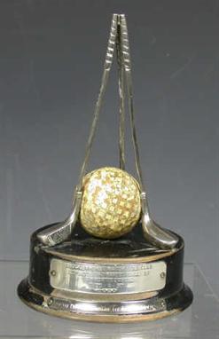 A Silvertown Golf Ball Co., hole-in-one trophy, formed as three upright clubs and a mesh-patterned golf ball, on an  ebonised