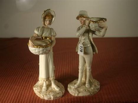 A pair of Royal Worcester cream glazed figurines, one of a standing peasant boy carrying a woven basket on his shoulder and t