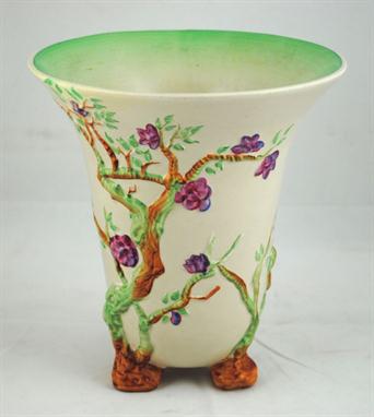 A Clarice Cliff cream glaze vase of tapering trumpet form with trees and blossom in polychrome relief and raised on 3 natural